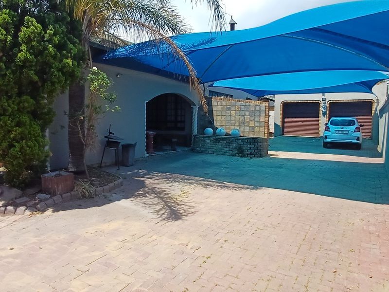 Front exterior view featuring a paved driveway, double garage, and a large blue shade sail covering the parking area.