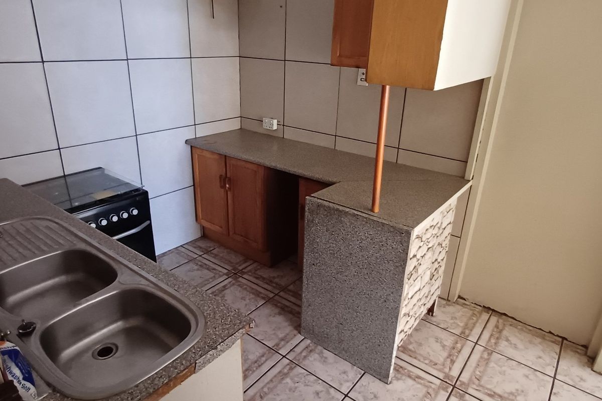 A compact kitchen featuring tiled flooring, a double bowl sink, laminate countertops, and built-in cabinetry with a tiled backsplash.