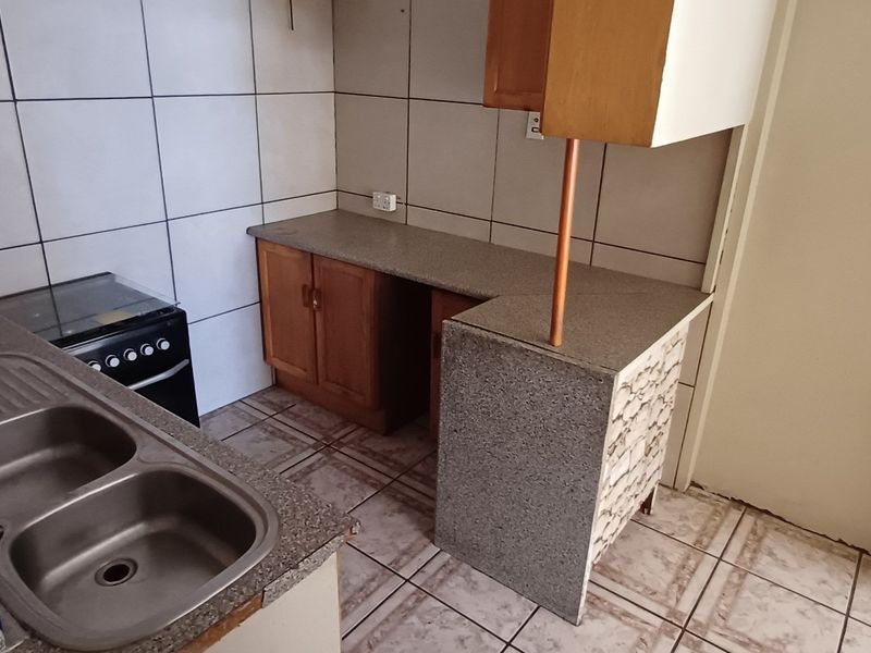 A compact kitchen featuring tiled flooring, a double bowl sink, laminate countertops, and built-in cabinetry with a tiled backsplash.