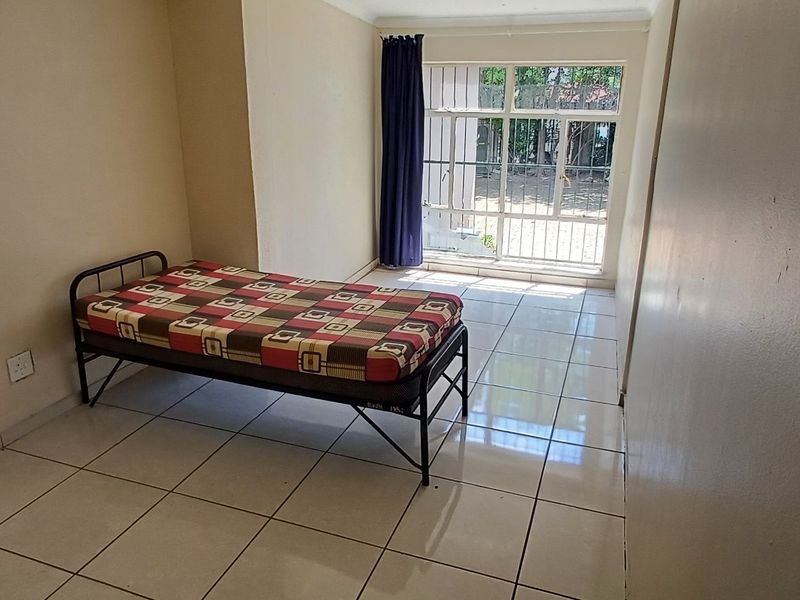 A simple bedroom featuring tiled flooring and a sliding glass door with a security gate, providing direct access to the exterior.