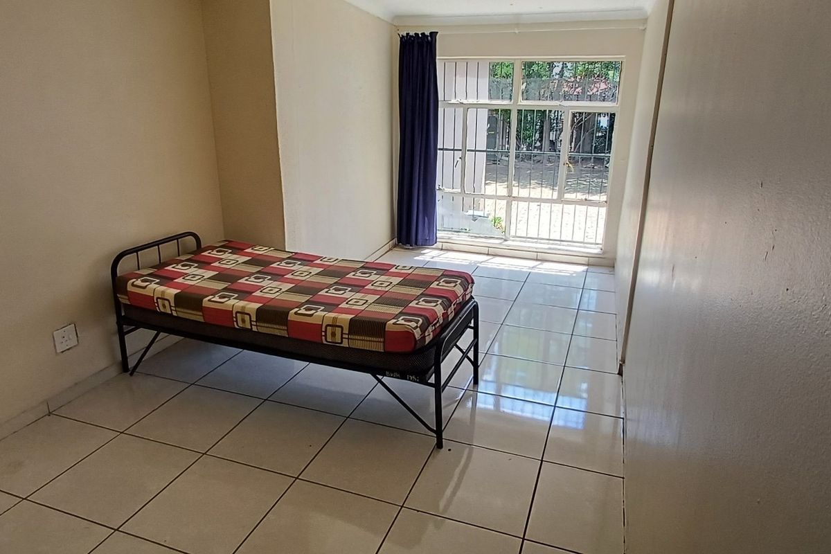 A simple bedroom featuring tiled flooring and a sliding glass door with a security gate, providing direct access to the exterior.