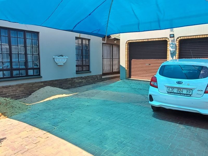 Front exterior view featuring a paved driveway, double garage with roller doors, and a large blue shade sail covering the parking area.