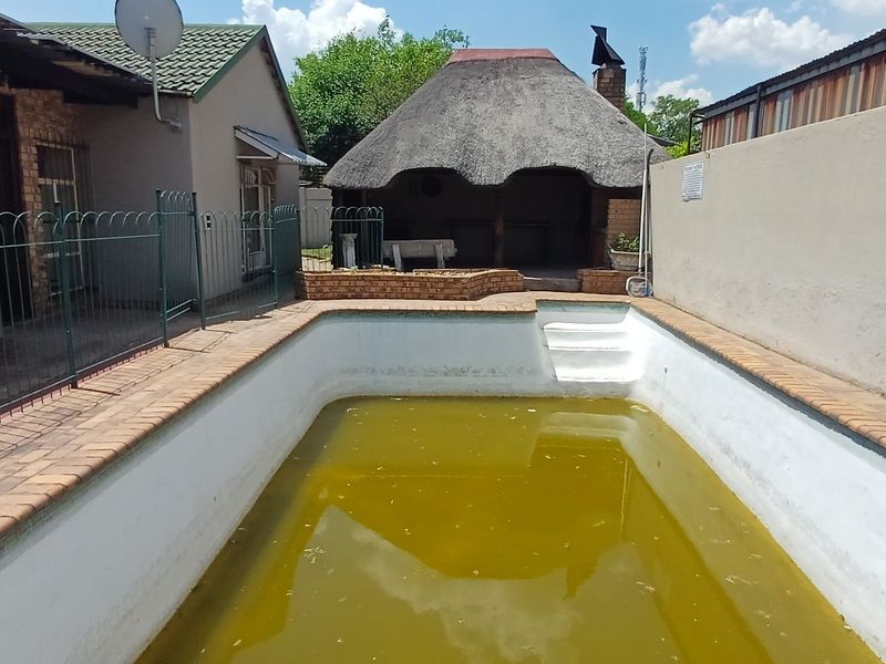 Outdoor pool area featuring a swimming pool, brick boundary wall, and a thatched lapa structure in the background.