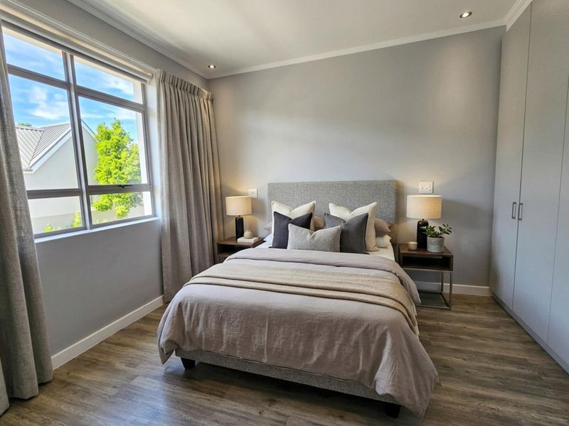 A well-maintained bedroom featuring modern laminate flooring, built-in cupboards, recessed downlighting, and a large window providing natural light.