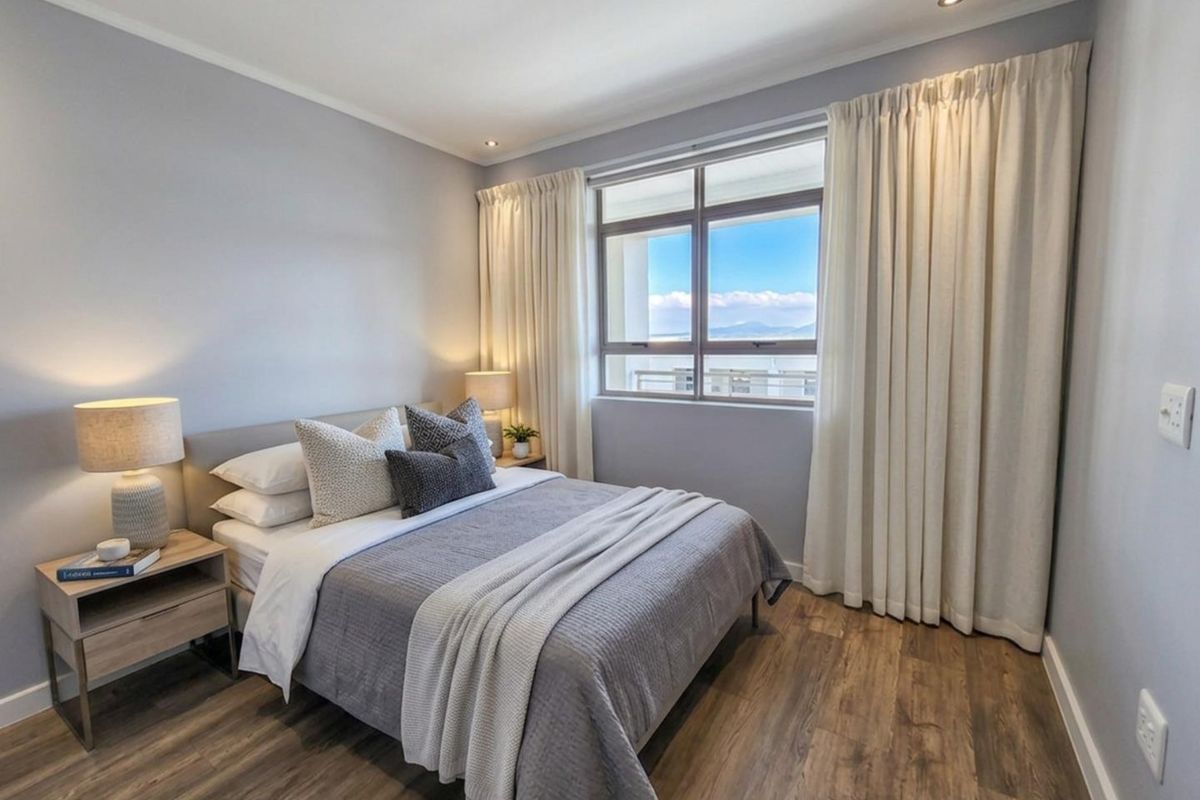 A well-maintained bedroom featuring modern laminate flooring, recessed ceiling lighting, and a large window with natural light and scenic views.