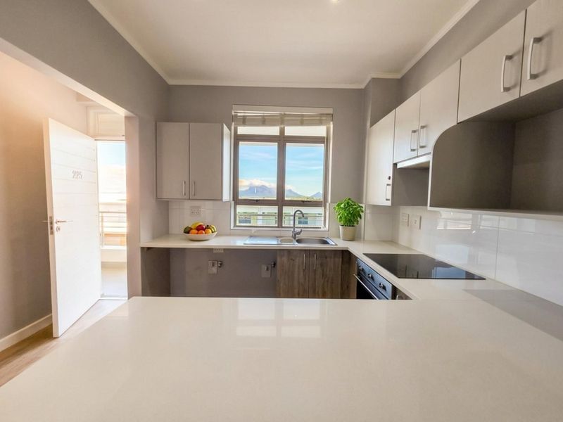 Modern kitchen featuring sleek white cabinetry, stone countertops, integrated hob and oven, and a window offering scenic mountain views.