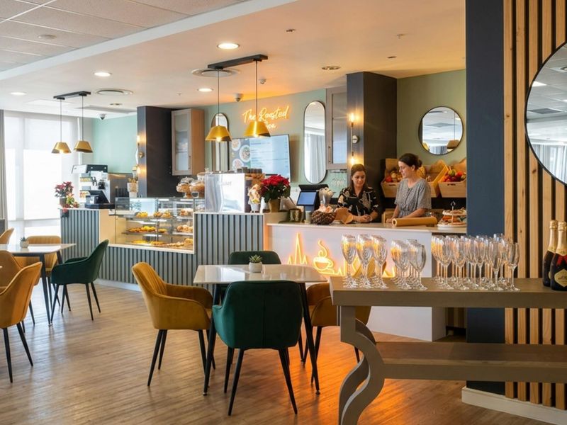 A modern, well-maintained open-plan cafe area featuring a professional service counter, stylish pendant lighting, and warm laminate flooring.