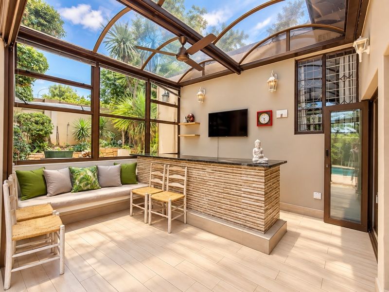 A bright, enclosed patio featuring a curved glass roof, built-in bar counter, and integrated bench seating, offering a seamless transition to the garden area.