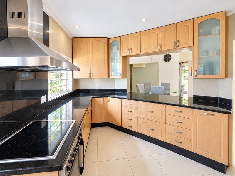 A well-maintained kitchen featuring light wood cabinetry, black granite countertops, a built-in electric hob, and a convenient pass-through window to the dining area.