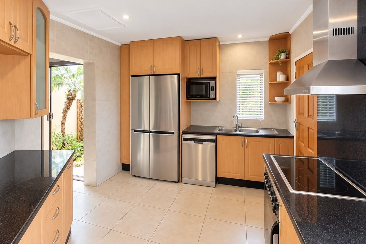 Well-appointed kitchen featuring light wood cabinetry, granite countertops, stainless steel appliances, and direct access to an outdoor area.