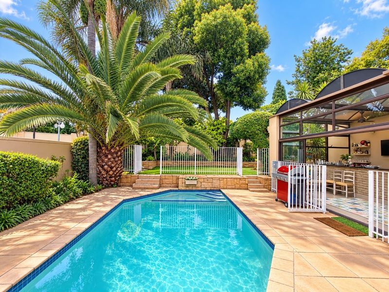 A well-maintained outdoor pool area featuring a tiled surround, retaining wall, and a covered patio space with glass sliding doors.