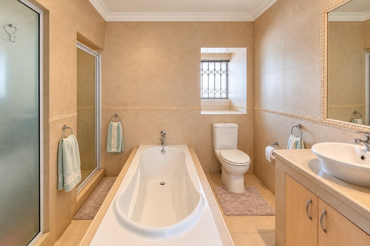 A well-maintained bathroom featuring a built-in bathtub, separate shower enclosure, vanity with vessel sink, and neutral floor-to-ceiling tiling.