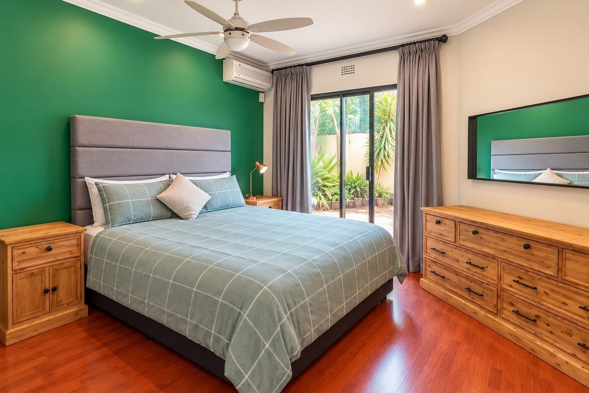 A well-maintained bedroom featuring laminate flooring, a ceiling fan, split system air conditioning, and direct access to the garden through sliding glass doors.