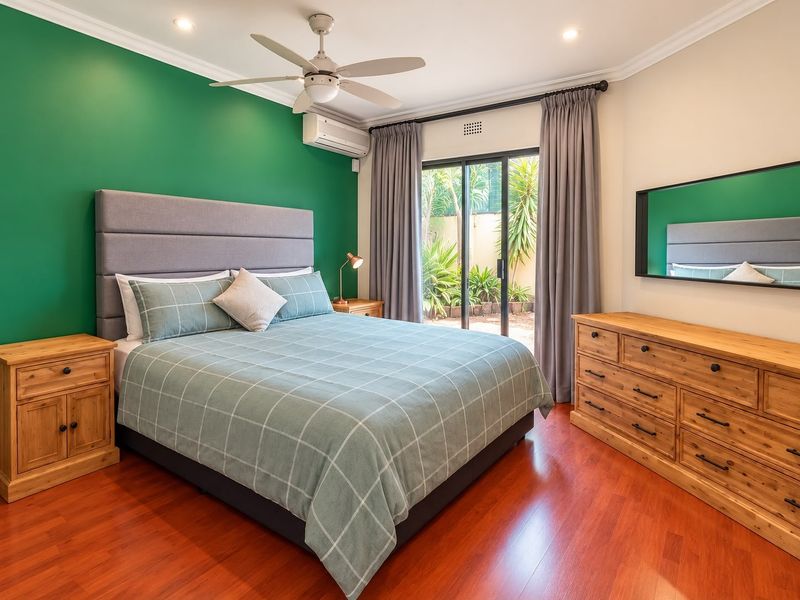 A well-maintained bedroom featuring laminate flooring, a ceiling fan, split system air conditioning, and direct access to the garden through sliding glass doors.