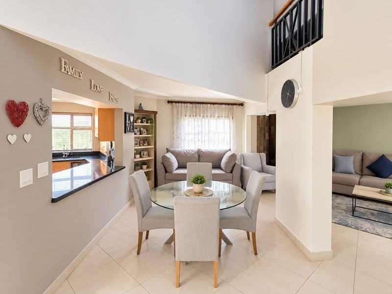 Spacious open-plan living and dining area featuring double-volume ceilings, tiled flooring, and a mezzanine level overlooking the main living space.