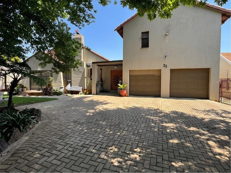 Front view of the property featuring a paved driveway, double garage, and a covered entrance area with established garden surroundings.