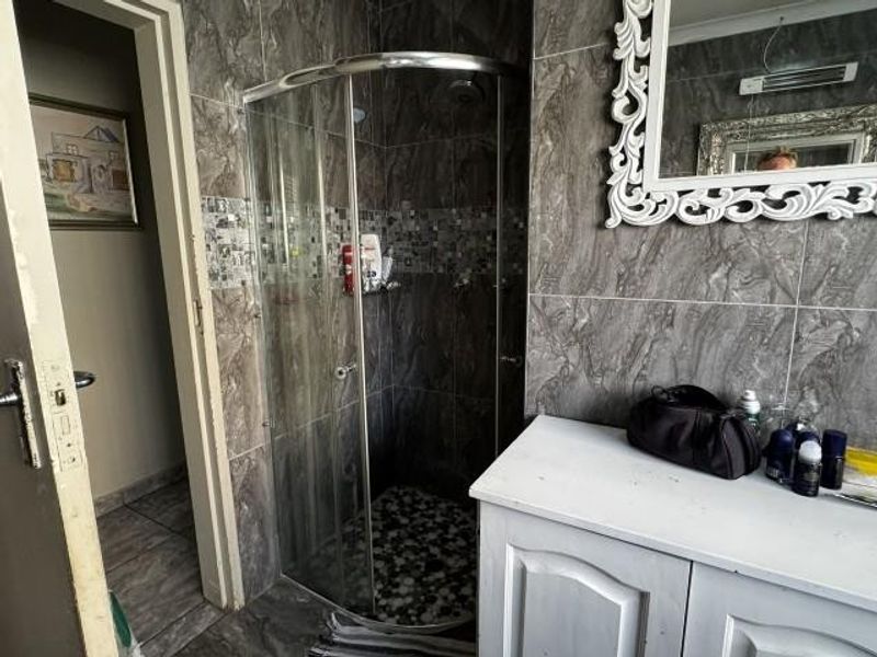 A bathroom featuring a curved glass shower enclosure, tiled walls and flooring, and a vanity cabinet with a decorative mirror.