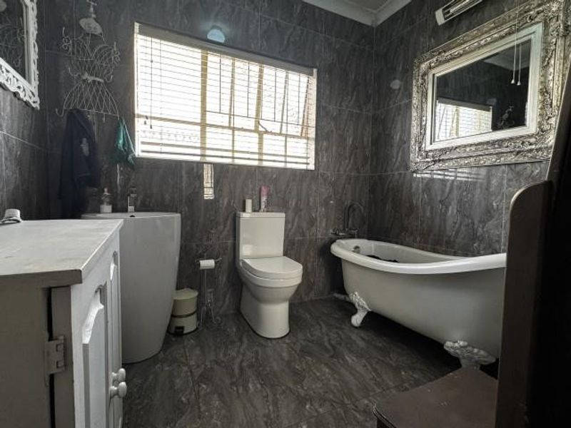 A modern bathroom featuring dark marble-effect wall and floor tiles, a classic clawfoot freestanding bathtub, a pedestal basin, and a white toilet.