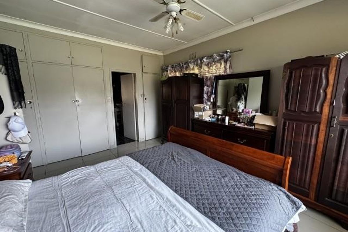 Spacious bedroom featuring extensive built-in cupboard storage, a ceiling fan, and tiled flooring, offering a functional layout with potential for modernization.
