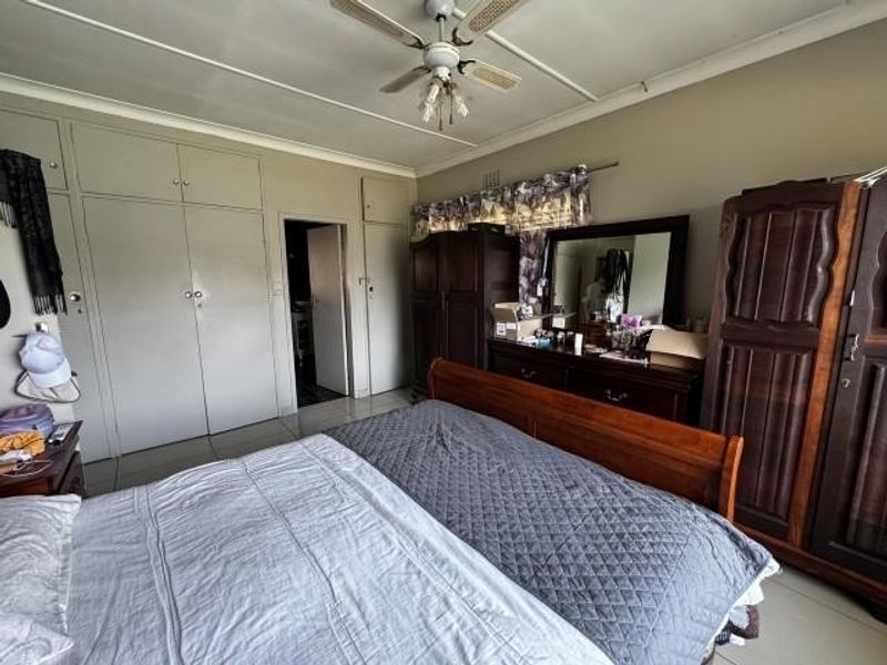 Spacious bedroom featuring extensive built-in cupboard storage, a ceiling fan, and tiled flooring, offering a functional layout with potential for modernization.