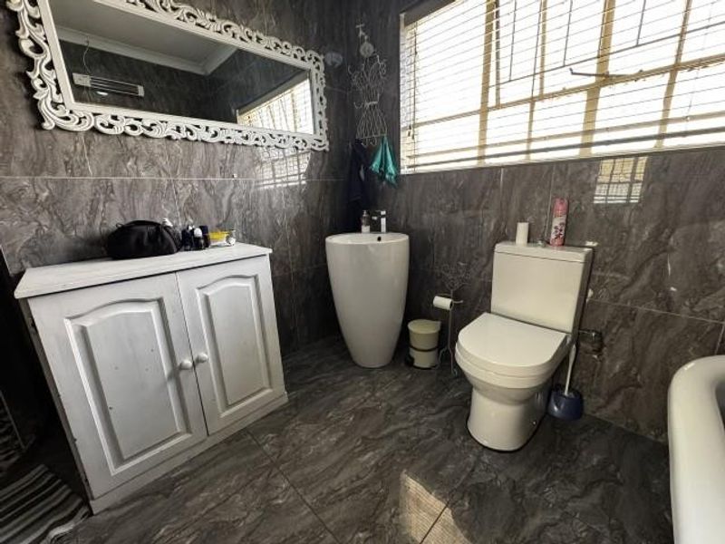 A bathroom featuring dark marble-effect wall and floor tiles, a white vanity cabinet, a modern pedestal basin, and a standard toilet.