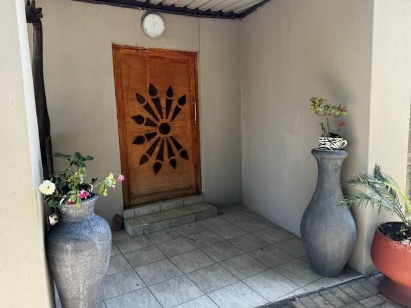 A covered entrance area featuring tiled flooring and a decorative wooden front door, providing a welcoming access point to the home.