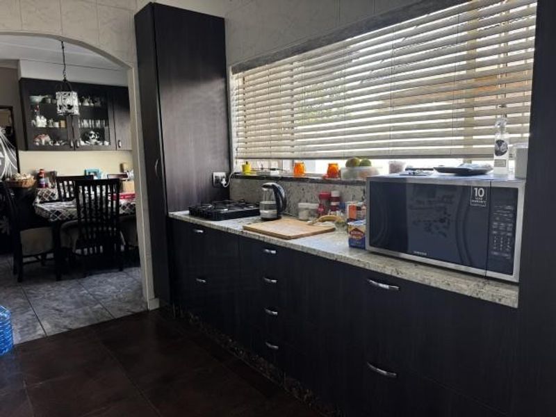 A functional kitchen featuring dark wood cabinetry, granite countertops, a gas hob, and a built-in microwave, with an adjacent dining area visible through an archway.