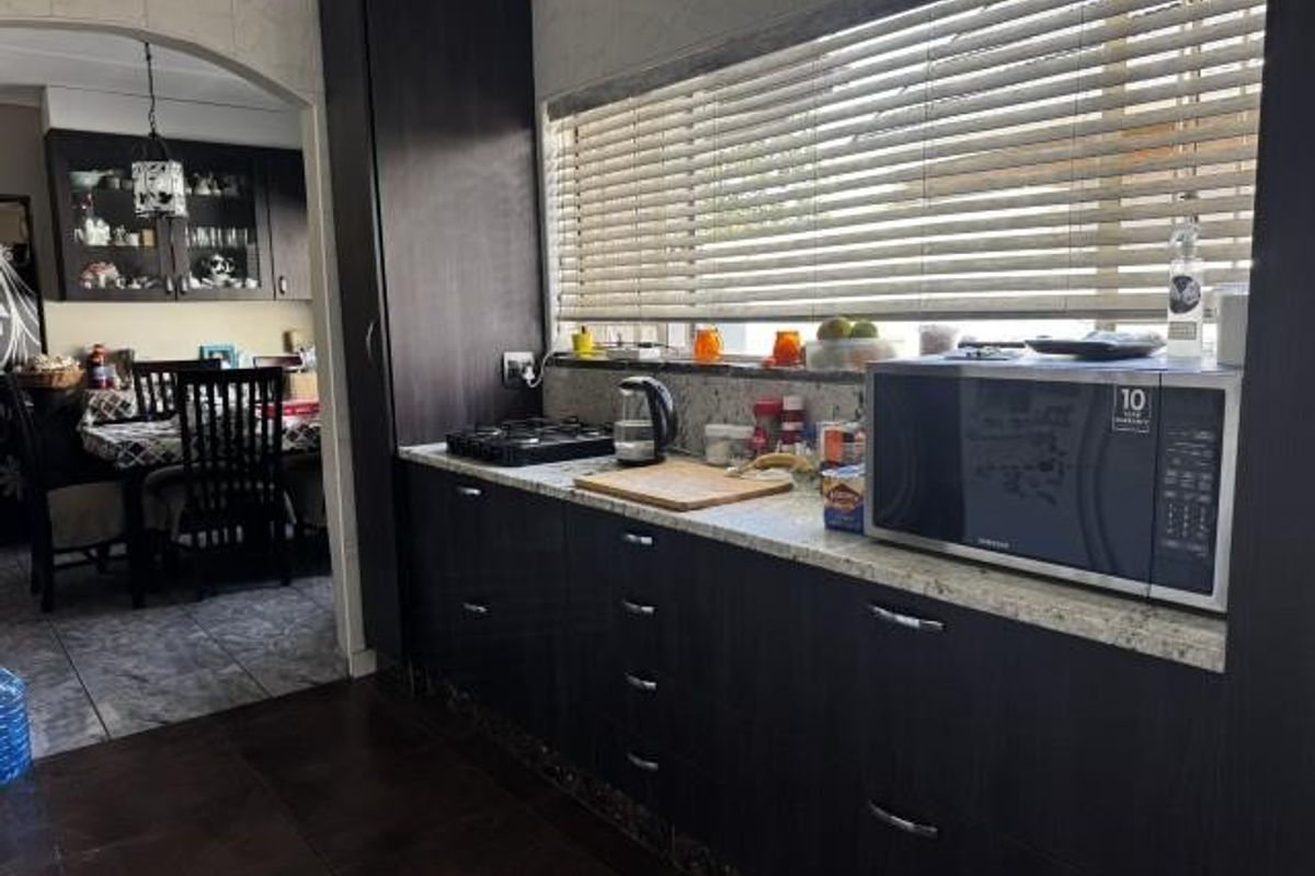 A functional kitchen featuring dark wood cabinetry, granite countertops, a gas hob, and a built-in microwave, with an adjacent dining area visible through an archway.