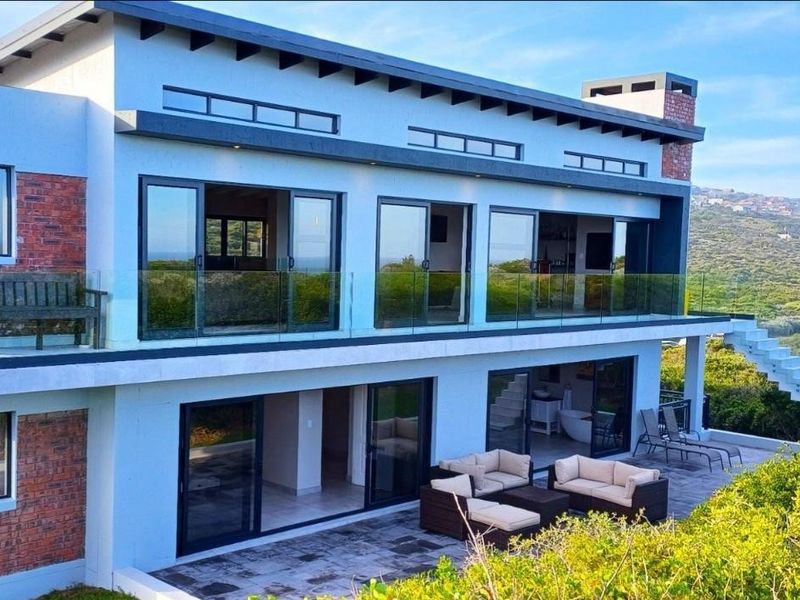 Modern multi-level residence featuring expansive glass sliding doors, glass balustrades, and a spacious rear patio overlooking natural landscape.