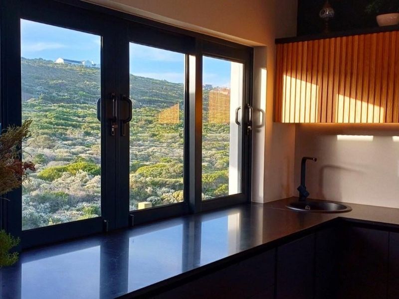Modern kitchen featuring sleek black countertops, slatted timber cabinetry with integrated lighting, and large windows offering scenic hillside views.