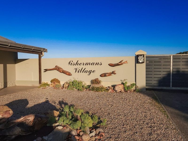 Front entrance area of Fishermans Village featuring a decorative boundary wall, gravel driveway, and gated access with landscaped garden elements.