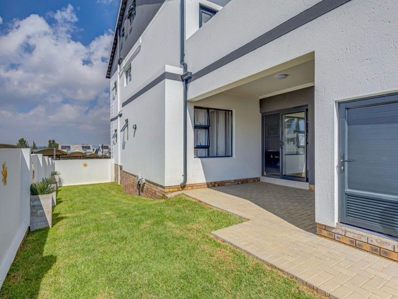 A well-maintained rear exterior view featuring a paved patio area, a small lawn, and modern sliding glass doors leading into the apartment.