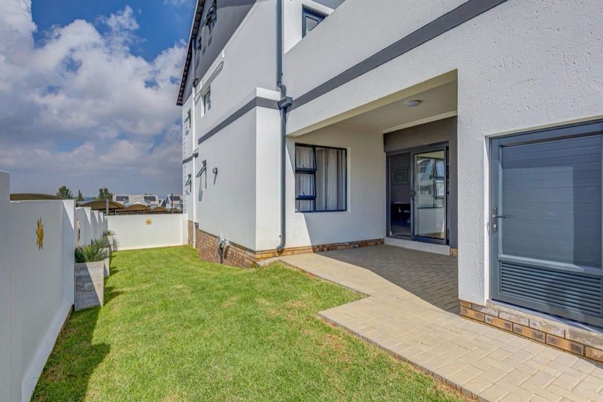 A well-maintained rear exterior view featuring a paved patio area, a small lawn, and modern sliding glass doors leading into the apartment.