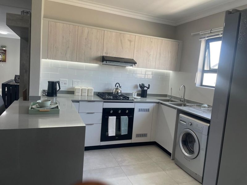 Modern kitchen featuring light wood-tone upper cabinets, sleek white lower cabinetry, stone countertops, subway tile backsplash, and integrated gas hob and oven.