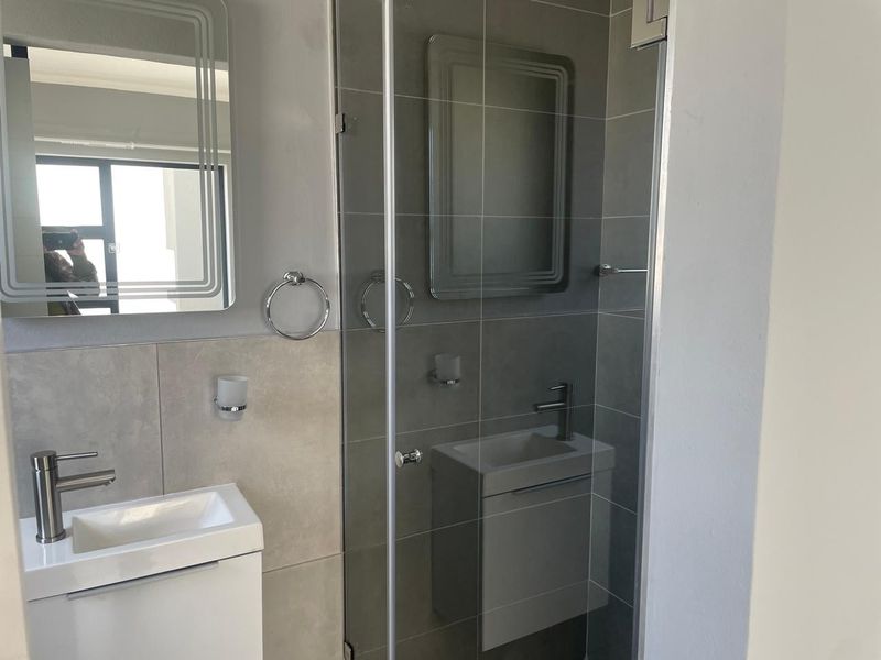 Modern bathroom featuring a sleek vanity with basin, mixer tap, and a glass-enclosed shower with contemporary grey wall tiling.