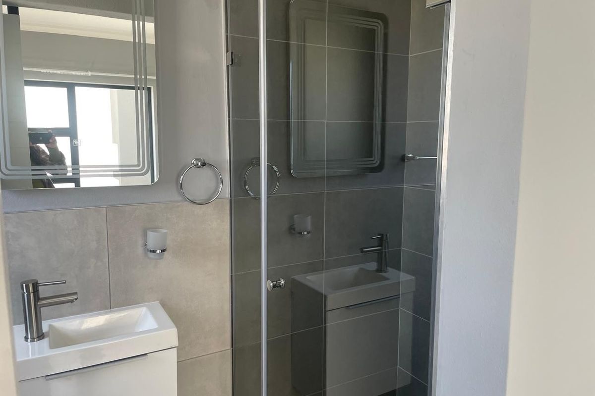 Modern bathroom featuring a sleek vanity with basin, mixer tap, and a glass-enclosed shower with contemporary grey wall tiling.