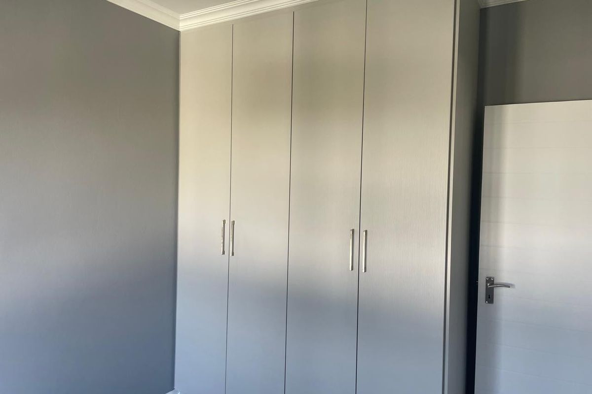 A clean, modern bedroom featuring neutral grey walls and floor-to-ceiling built-in cupboards with contemporary hardware.