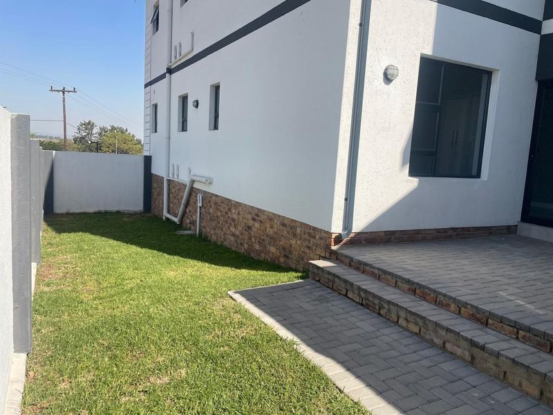 A side view of the apartment building featuring a paved patio area, a small lawn, and a secure boundary wall.