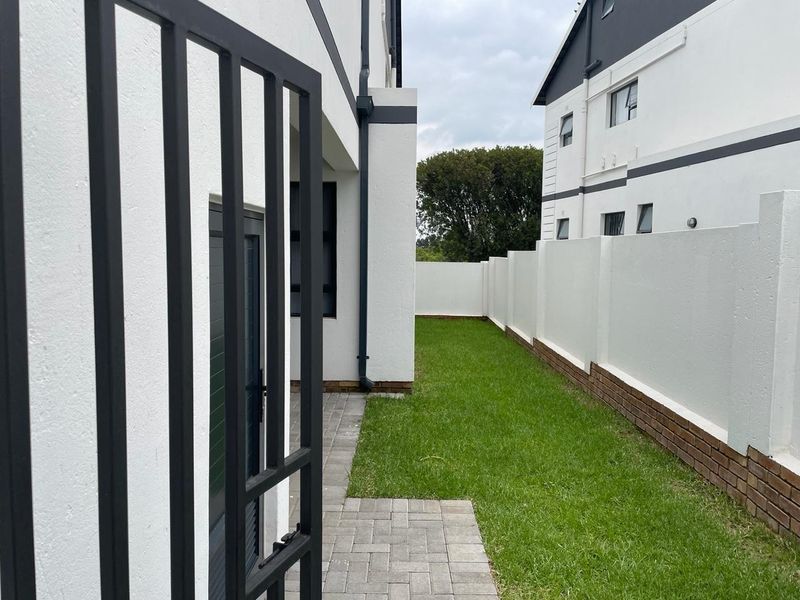 A well-maintained rear garden area featuring a neat lawn, paved walkway, and secure boundary walling, providing a private outdoor space.