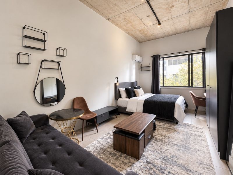 Modern open-plan studio apartment featuring an exposed concrete ceiling, large window for natural light, and built-in storage.