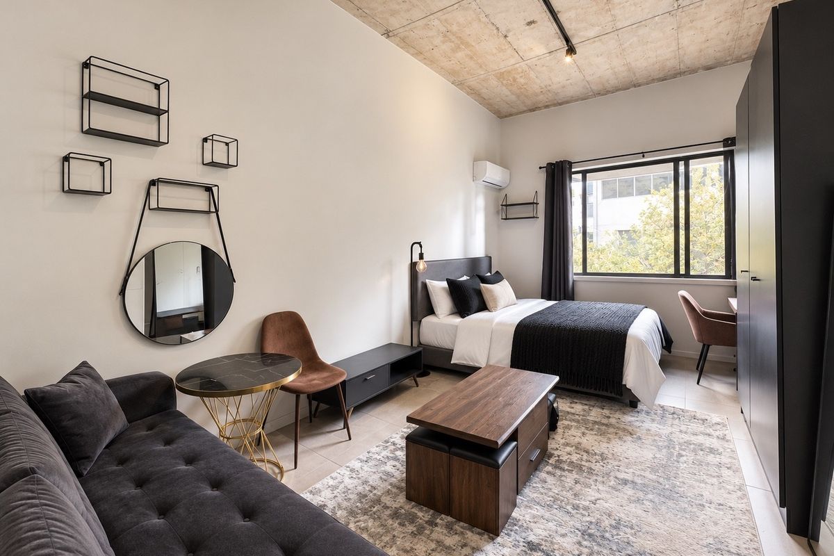 Modern open-plan studio apartment featuring an exposed concrete ceiling, large window for natural light, and built-in storage.
