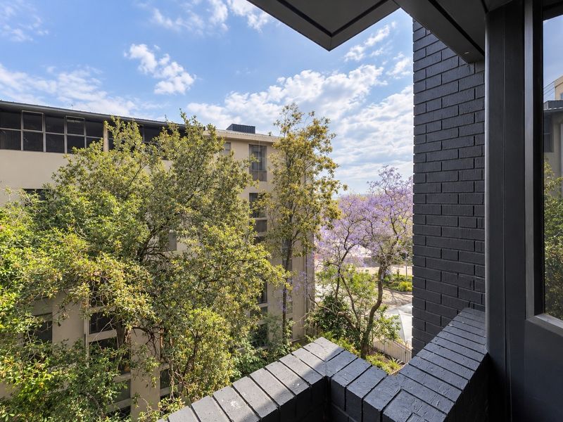 A private balcony featuring a dark brick balustrade with an elevated view of the surrounding neighbourhood and mature trees.