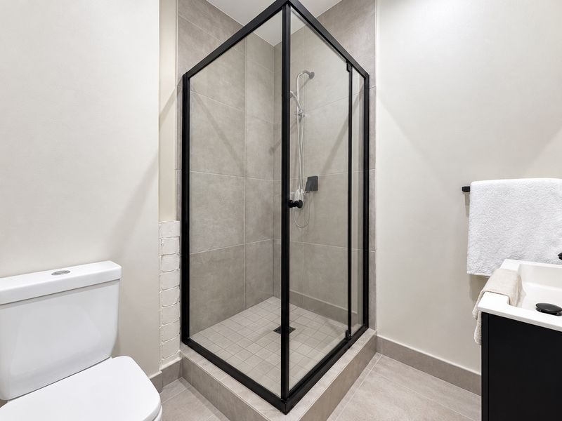 Modern bathroom featuring a sleek glass shower enclosure with black framing, a contemporary vanity, and neutral floor-to-ceiling tiling.