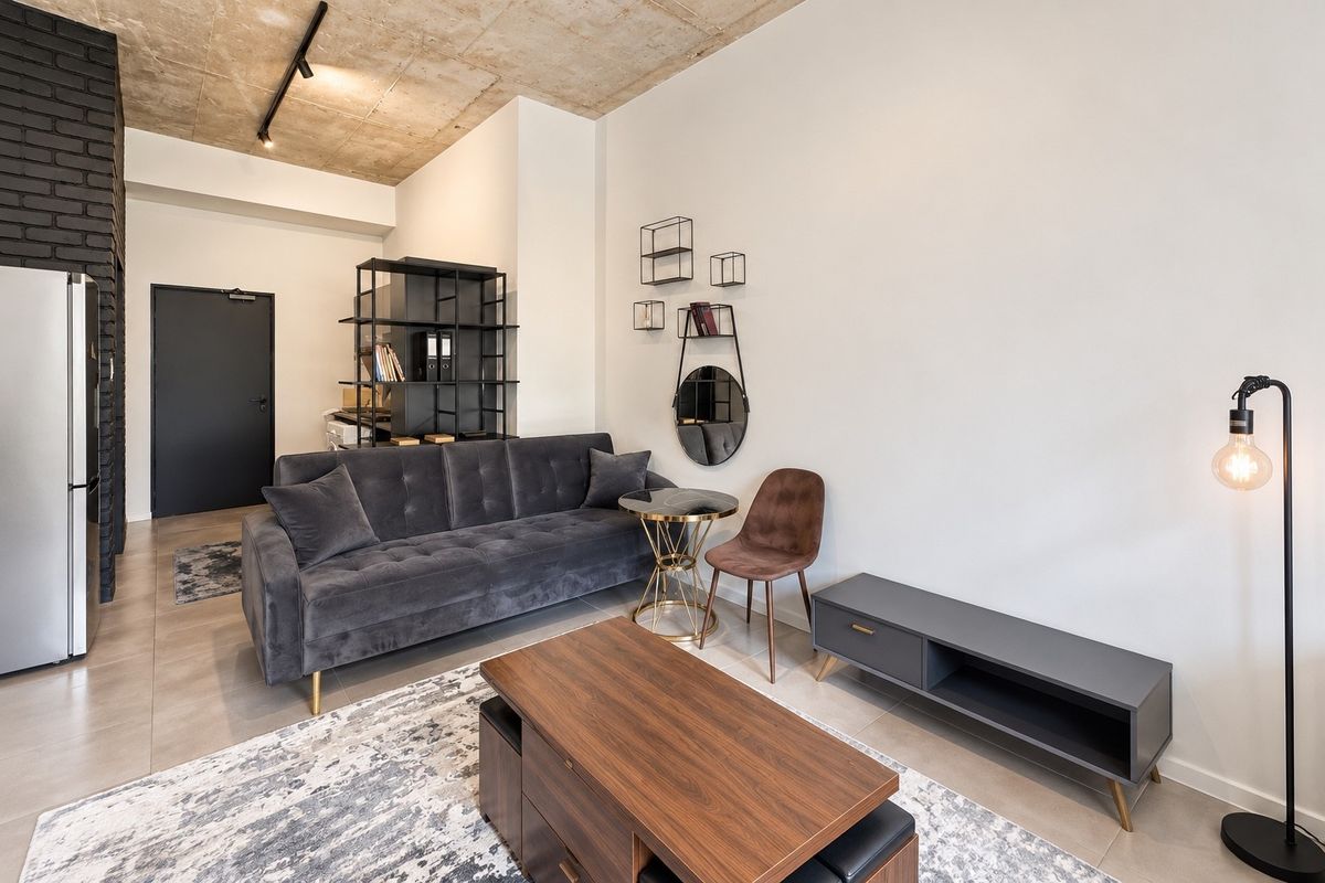 Modern living room featuring an exposed concrete ceiling, sleek tiled flooring, and a striking black brick accent wall, creating a contemporary industrial aesthetic.