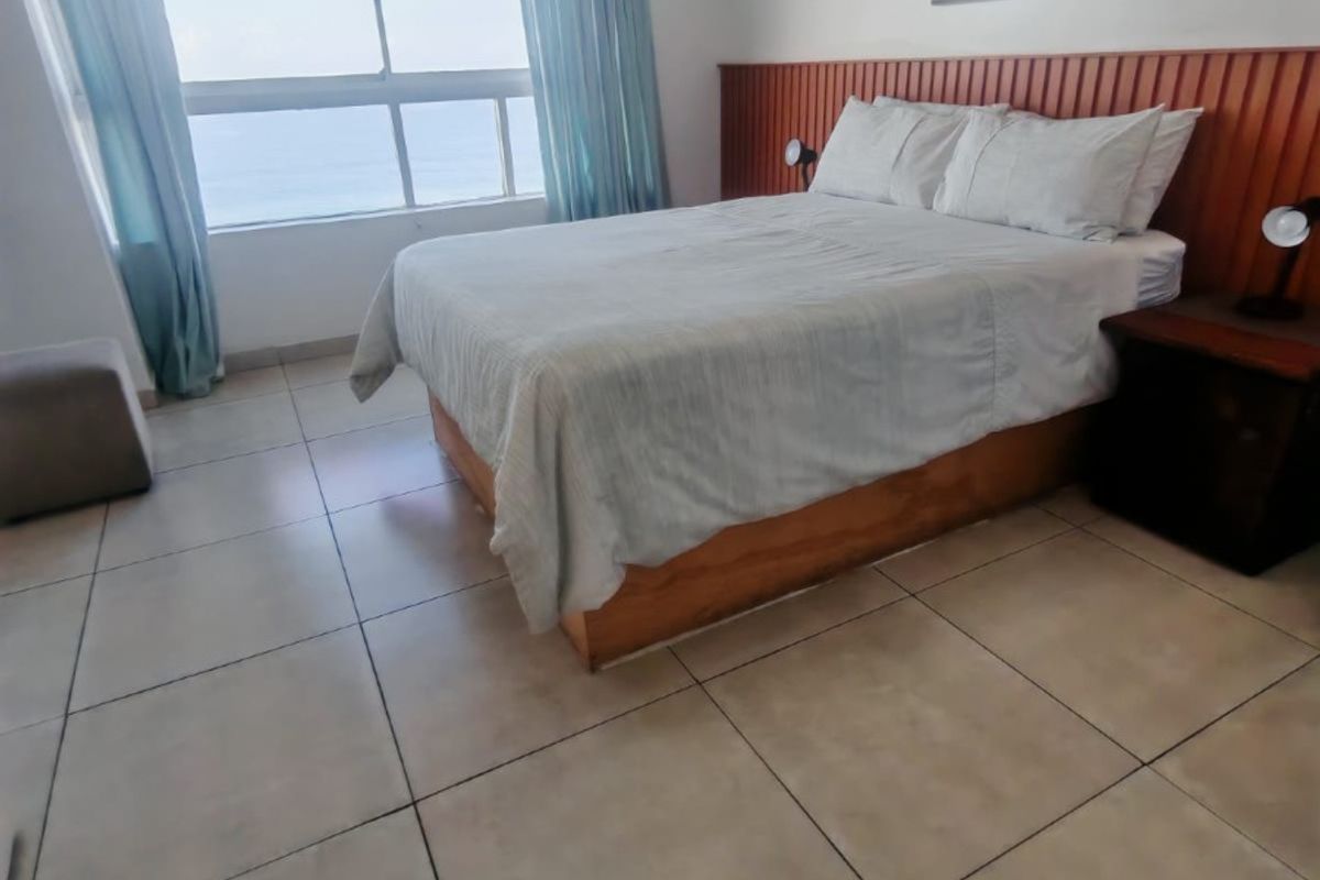 A bedroom featuring tiled flooring, a wooden headboard wall panel, and a large window with ocean views.