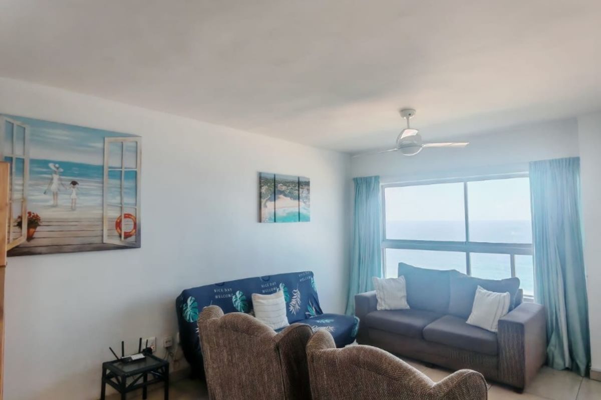 A bright living room featuring tiled flooring, a ceiling fan, and a large window offering expansive ocean views.