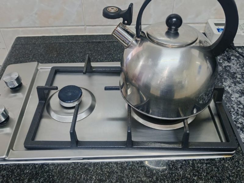 Close-up view of a stainless steel gas hob set into a dark granite countertop with a tiled backsplash.