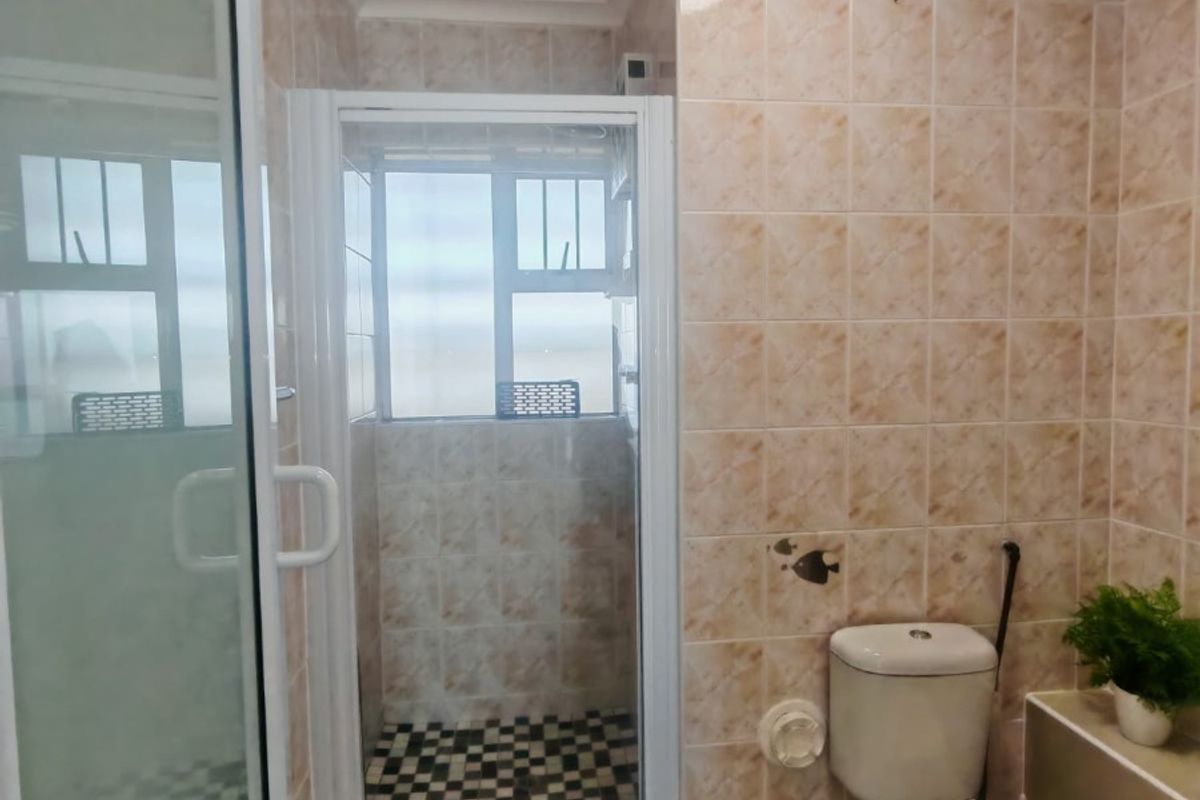 A functional bathroom featuring a shower enclosure, toilet, and neutral wall tiling, offering a practical layout with natural light from the window.