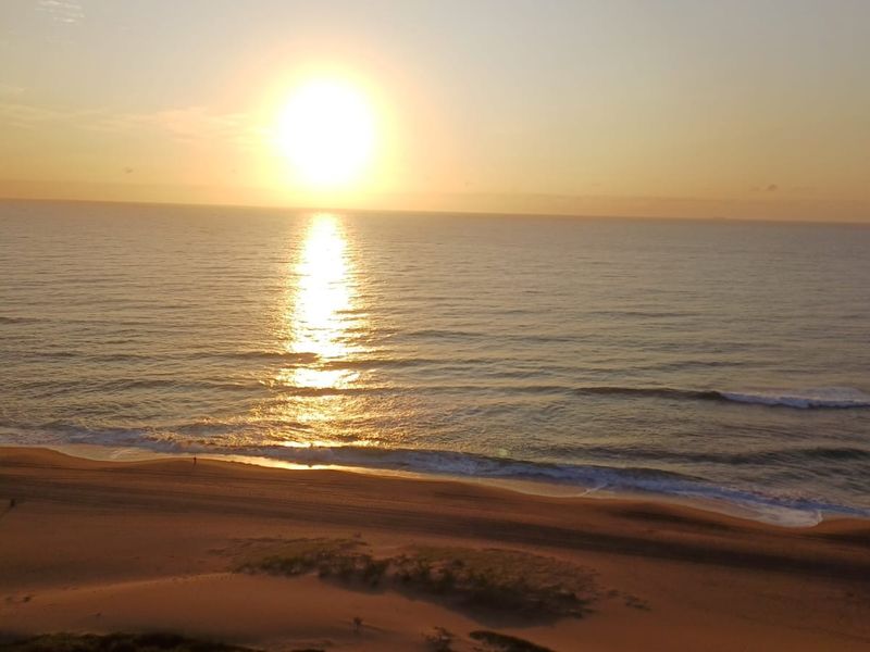 A scenic view of the ocean and sandy beach at sunrise, captured from an elevated position.