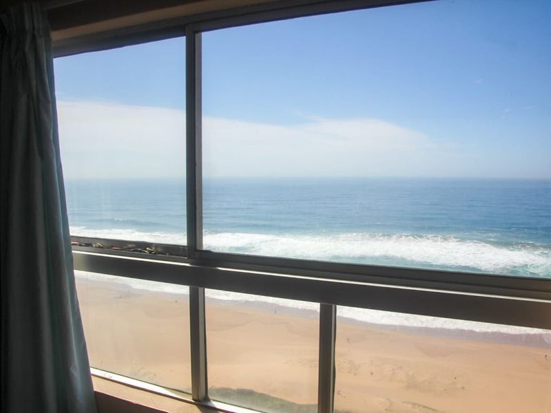 A clear, elevated view of the ocean and sandy beach captured through a large sliding window.